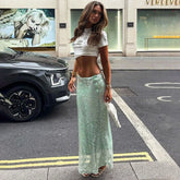 Woman in a white crop top and green sequin skirt standing on a city street.